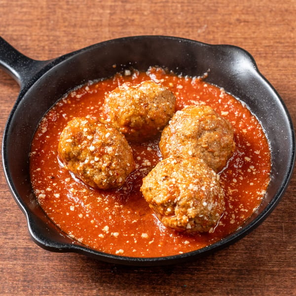 Four Grampie's Pizzeria meatballs in rich red sauce, topped with grated cheese in a black skillet.