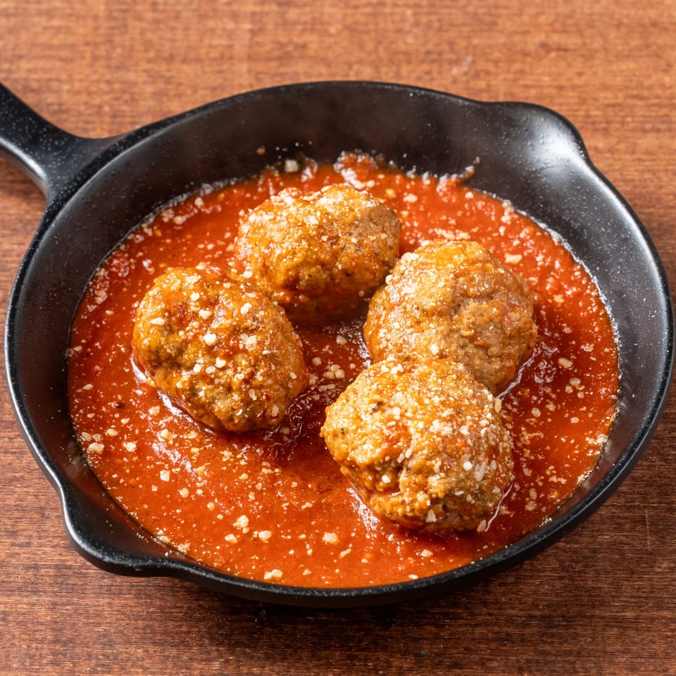 Four Grampie's Pizzeria meatballs in rich red sauce, topped with grated cheese in a black skillet.