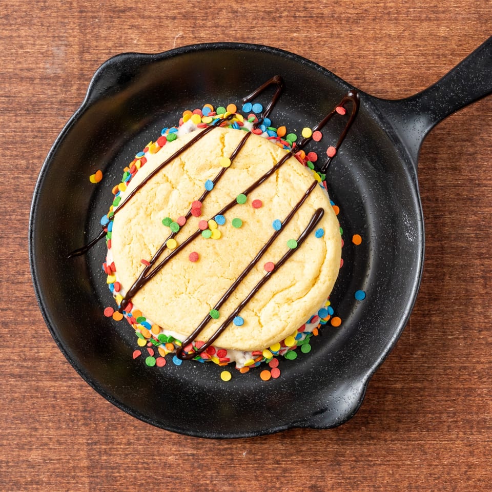 A Grampie's Pizzeria dessert: a large cookie sandwich with sprinkles and chocolate drizzle in a skillet.