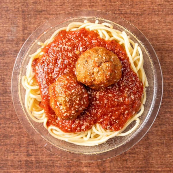 Spaghetti with two large meatballs and marinara sauce, topped with grated cheese in a clear bowl.