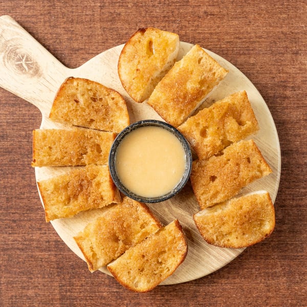 Grampie's Pizzeria's cinnamon sugar breadsticks with a side of sweet dipping sauce on a wooden board.