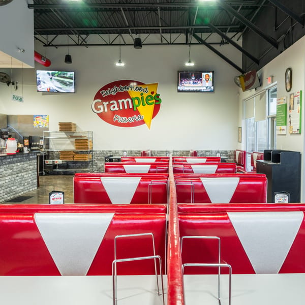Interior of Grampie's Pizzeria with red and white booths, a counter, and the restaurant logo.