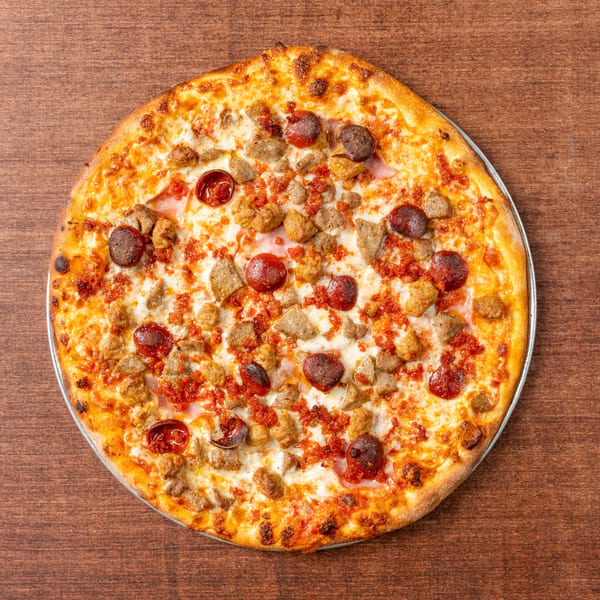 Grampie's Pizzeria's meat lover's pizza, topped with pepperoni, sausage, and bacon, on a wooden table.