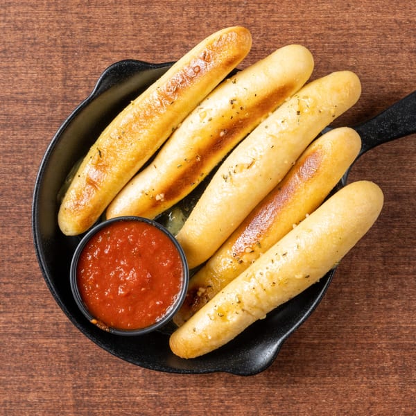 Golden-brown Grampie's Pizzeria breadsticks with herbs and garlic, served with a side of marinara sauce.
