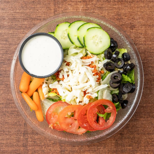 A fresh garden salad with lettuce, tomatoes, cucumbers, olives, carrots, cheese, and dressing.
