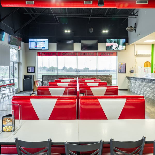 Interior of Grampie's Pizzeria with red and white booths, tables, and TVs showing sports.