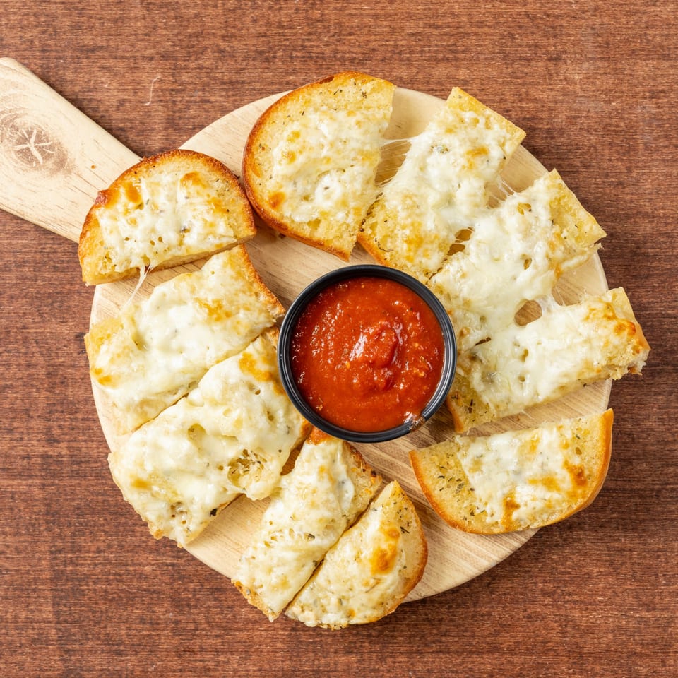 Cheesy garlic bread slices with melted mozzarella and herbs, arranged around a bowl of marinara sauce.