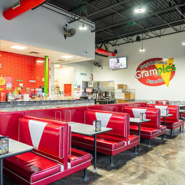 Interior of Grampie's Pizzeria with red booths, tables, a counter, and the restaurant logo on the wall.