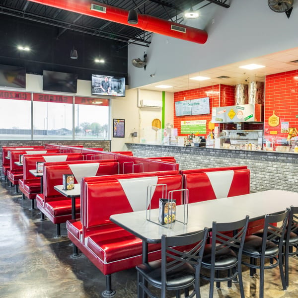 Interior of Grampie's Pizzeria with red and white booths, tables, and a counter with pizza ovens.